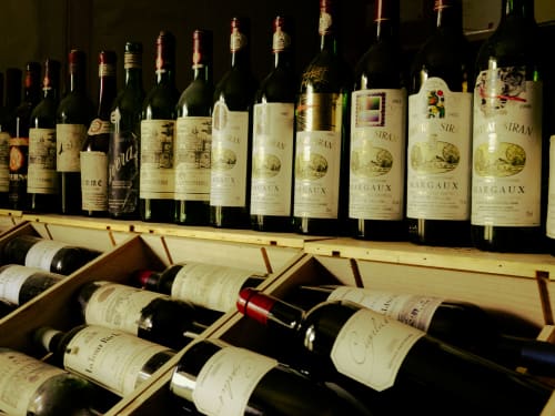 Wine collection display at La Guirtelle B&B in Lainsecq, France with vintage Margaux bottles and wooden racks.