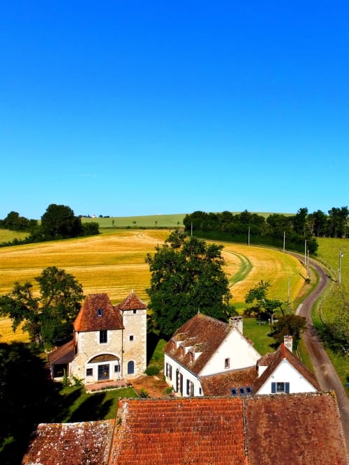 La Guirtelle B&B in Lainsecq, France: Stone farmhouse with red tile roof among rolling golden fields and green countryside.