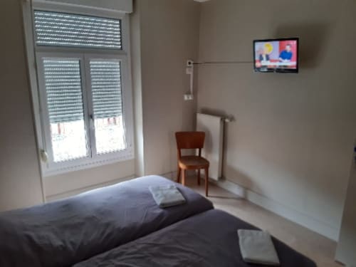 Chambre standard de la Résidence Soanska du Gérardmer avec lit, TV, chaise en bois et fenêtre donnant sur la ville