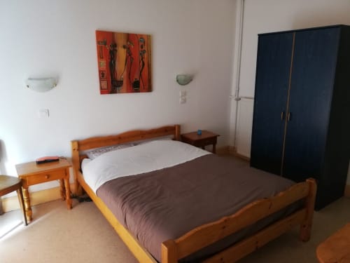 Chambre standard de la Résidence Soansa du Gérardmer avec lit en bois, armoire foncée et tableaux sur murs blancs