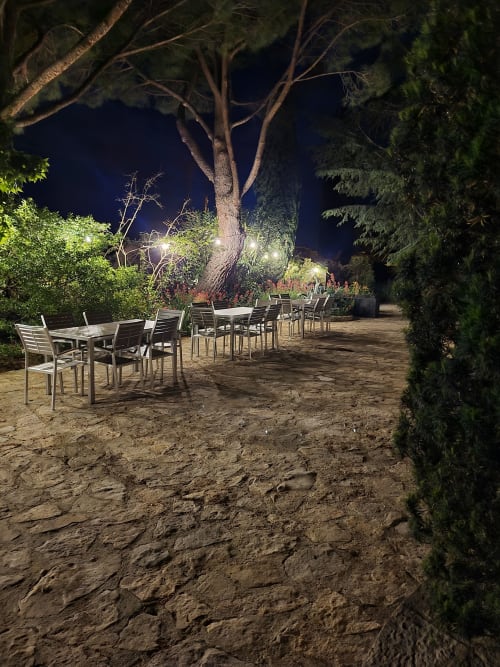 Nächtliche Terrasse der Villa Thébaïde mit Esstischen und Stühlen unter beleuchteten Bäumen in Laudun L'Ardoise