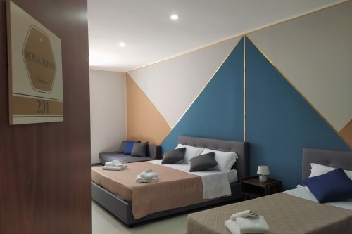 Modern hotel room at Royal Rooms Station Napoli with geometric blue accent wall, dual beds, and contemporary furnishings