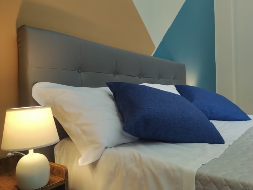Modern bedroom at Royal Rooms Station Napoli with gray headboard, navy pillows, white bedding, and geometric wall art