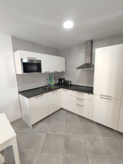 Moderna cocina blanca con encimeras negras y electrodomésticos de acero inoxidable en el apartamento El Faro De Los Genoveses en San José.