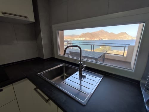 Cocina moderna con vistas al mar en El Faro De Los Genoveses, Almería. Encimera negra, fregadero de acero inoxidable, ventanal con vistas