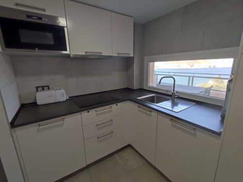 Cocina moderna blanca con encimeras negras y ventana con vistas al mar en El Faro De Los Genoveses, Almería