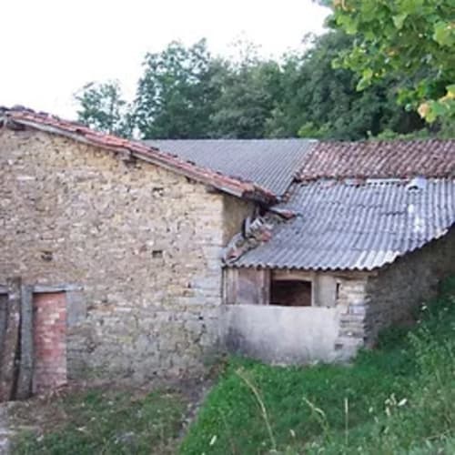 Edificio de piedra rústica con techo de chapa ondulada en Casa Lafuente, Lukiano, Araba, rodeado de vegetación verde