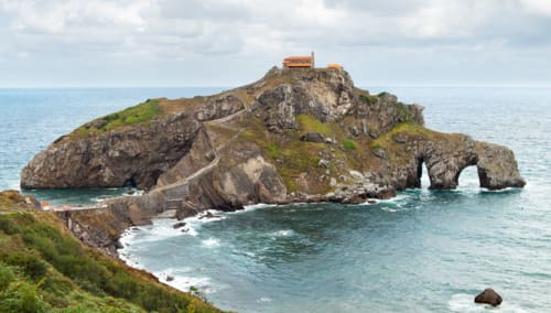 Isla rocosa de San Juan de Gaztelugatxe con construcción naranja y puente arqueado en el País Vasco, España