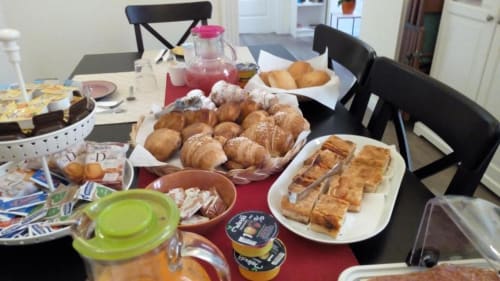 Mesa de desayuno en B&B Il Conservatorio Nápoles con pastelería, cruasanes, zumo de fruta y productos horneados sobre mantel rojo