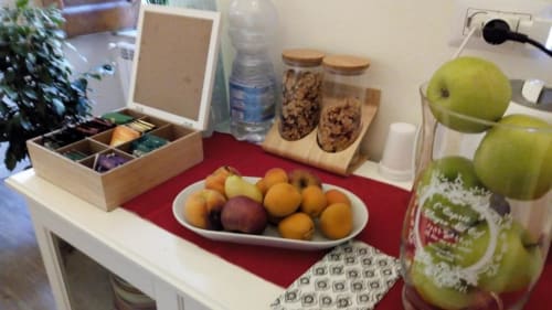 Mesa de bienvenida del B&B Il Conservatorio Nápoles con fruta fresca, cereales, agua y zumo de manzana sobre mantel rojo