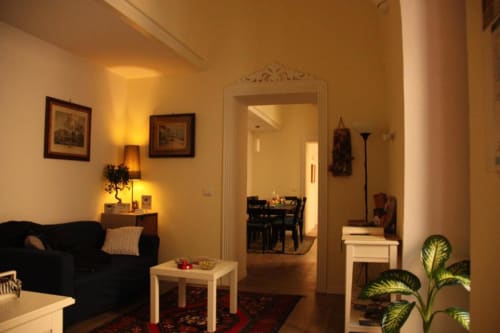 Warm lit living room at B&B Il Conservatorio Naples with black armchair, white table, and doorway to dining area