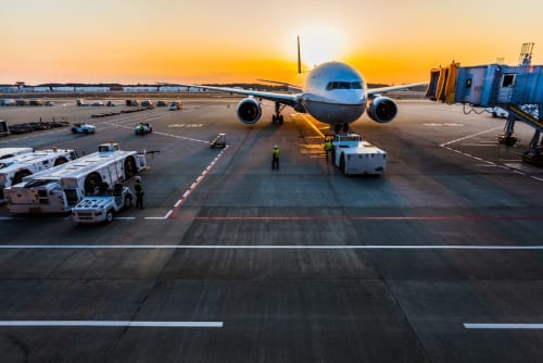 Commercial aircraft at sunrise on tarmac with ground support vehicles near Naples airport