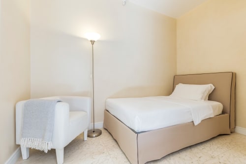 Camera da letto spaziosa negli Petra Apartments Rome con letto beige, poltrona bianca e arredi moderni