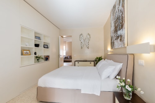 Camera da letto moderna e luminosa presso Petra Apartments Rome con letto matrimoniale, biancheria bianca, scaffalature integrate e vista sulla città dalla finestra