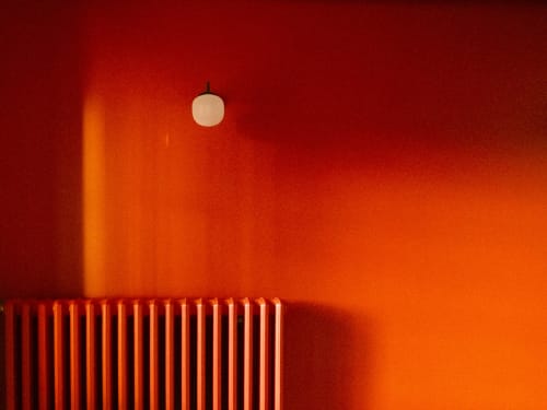 Intérieur minimaliste de la chambre d'hôtes La Guirtelle à Lainsecq avec murs rouge chaud, luminaire suspendu et radiateur