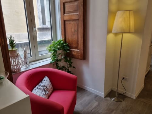 Cozy reading nook at B&B Il Conservatorio Naples with pink armchair, floor lamp, and potted plant by window