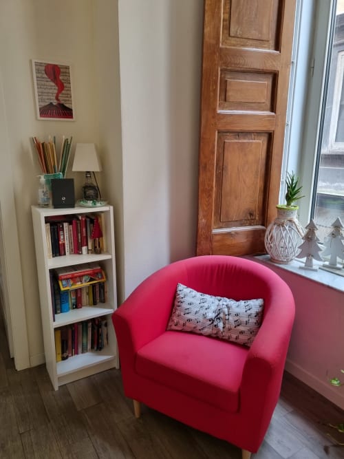 Cozy reading nook at B&B Il Conservatorio Naples with red armchair, bookshelf, and wooden door