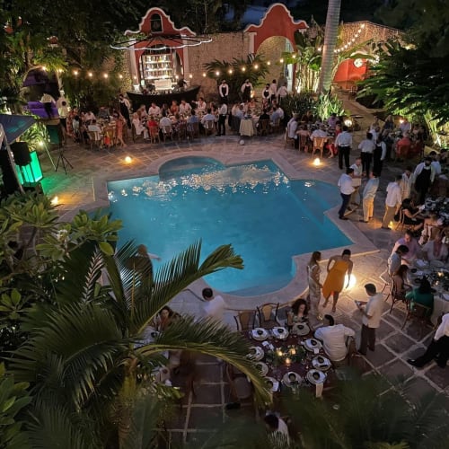 Baldoria notturna al Villa Merida Boutique Hotel. La foto ritrae la villa e l'area della piscina illuminate durante una vivace celebrazione, dove un raduno di persone aggiunge un'aria di gioia festosa all'incantevole ambiente circostante.