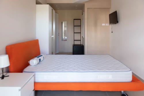 Camera moderna al Sicilianinsta Rooms B&B di Catania con letto arancione, materasso bianco e TV