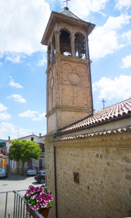 Antico campanile della chiesa di Filiano con muri in pietra e aperture ad arco contro il cielo azzurro