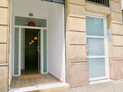 Modern apartment entrance at Mira Barna Barcelona with glass doors, white frame, and warm lighting inside