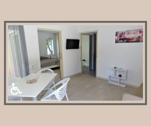 Séjour accessible de la Résidence Saint Michel à L'île Rousse, mobilier blanc, téléviseur et entrée de la chambre