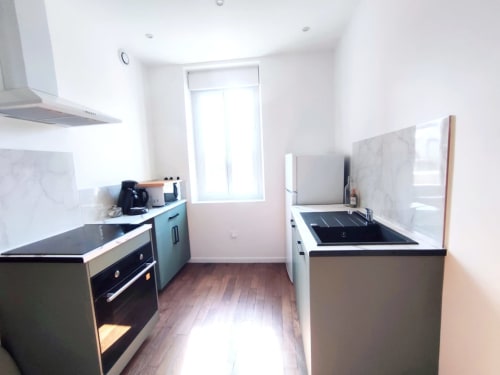 Cuisine moderne de l'appartement Lesdoucesnuits45 à Montargis avec armoires bleu canard, plans de travail noirs et appareils en acier inoxydable