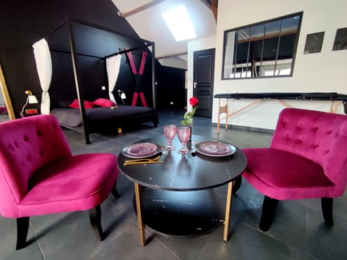 Élégant séjour de l'appartement Montargis avec fauteuils rose vif, table ronde noire et lit à baldaquin chez Lesdoucesnuits45