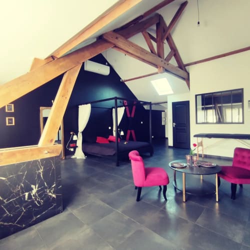 Élégant loft à Lesdoucesnuits45 à Montargis avec poutres en bois apparentes, chaises roses, sol foncé et