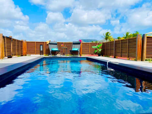 Piscine privée aux eaux turquoise, clôture en lames de bois, chaises longues et jardin tropical aux Hébergements Passion
