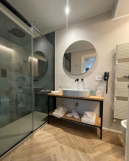 Bagno moderno a Covo del Pirata Venezia con specchio rotondo, lavabo bianco, doccia walk-in e mobile in legno