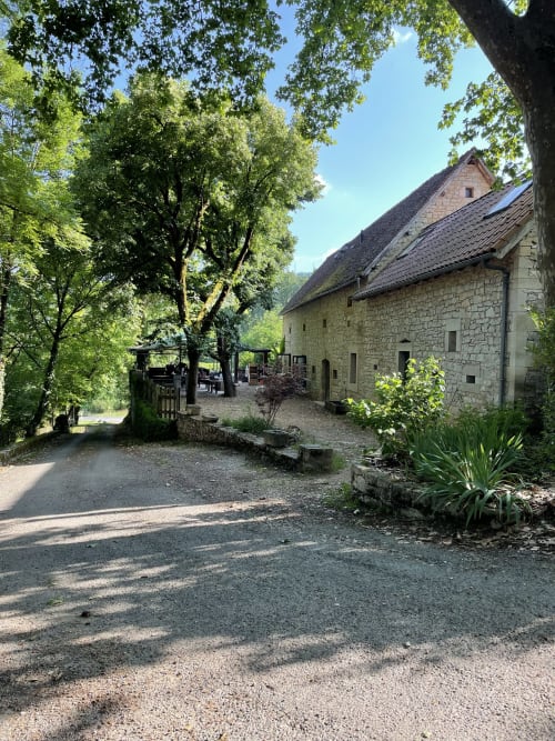Maison en pierre des Chambres d'hôtes Les Pratges à Figeac, entourée de jardins verdoyants et d'arbres, cour d'entrée rustique