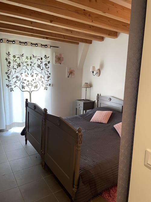 Chambre aux Chambres d'hôtes Les Pratges à Figeac avec poutres bois, lit sombre, coussins roses et rideaux botaniques