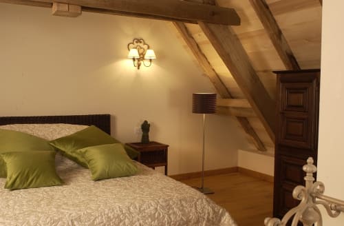 Chambre sous les toits douillette aux Chambres d'hôtes Les Pratges avec coussins verts, poutres apparentes, applique murale et porte en bois à Figeac