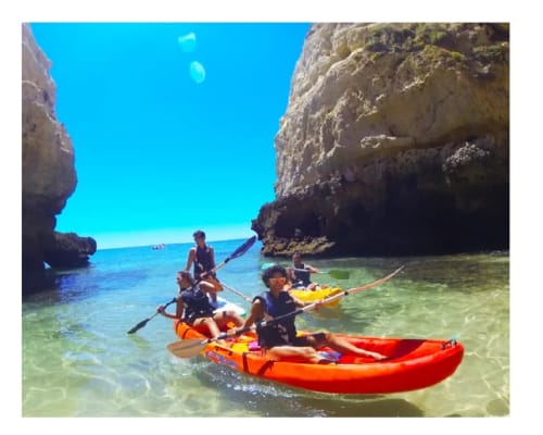 Kayakers paddling in crystal-clear turquoise waters near dramatic cliffs at Armação de Pêra beach, Portugal.