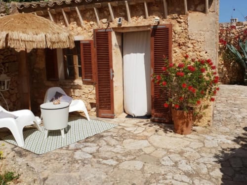 Terrasse rustique à Las Fincas De Annie à Felanitx avec volets rouges, chaise blanche et fleurs rouges éclatantes.