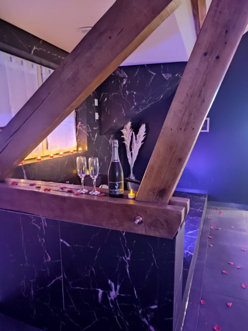 Élégante mise en place champagne à l'appartement Lesdoucesnuits45 : bar en marbre, poutres en bois, éclairage ambiant violet et pétales de roses