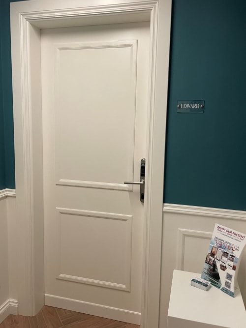 Porta in legno bianco con pannelli, denominata Edward in appartamento veneziano, dotata di serratura digitale e depliant informativo sul tavolo