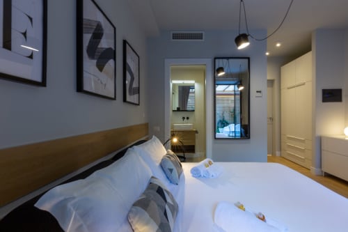 Camera moderna di Casa Lounge Istria a Cagliari con biancheria bianca, testata in legno, luci a sospensione e bagno ensuite