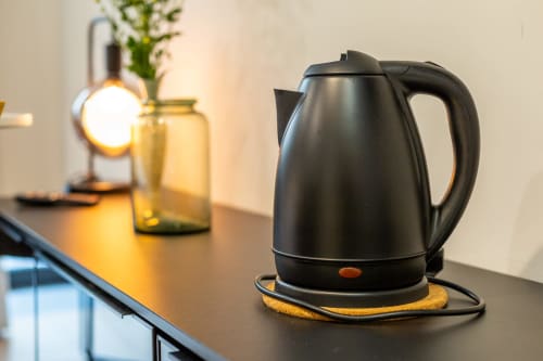 Bollitore elettrico nero su sottobicchiere in sughero alla scrivania della camera d'albergo Casa Lounge Istria, Cagliari