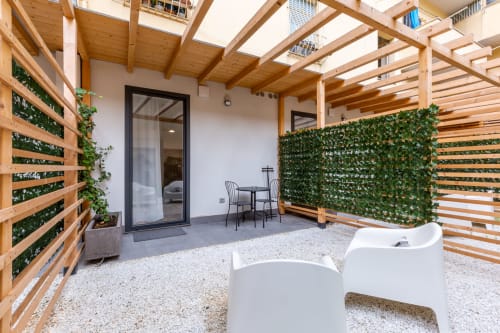 Terrazza moderna di Casa Lounge Istria a Cagliari con pergolato in legno, pareti verdi, sedute bianche e porte in vetro