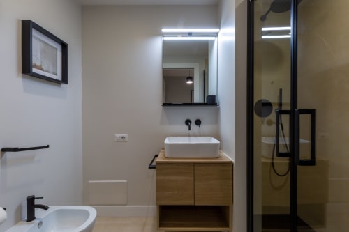 Bagno moderno di CASA LOUNGE ISTRIA a Cagliari con lavabo in ceramica bianca, vanità in legno, specchio e doccia in vetro