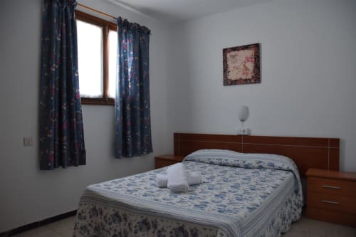 Acogedora habitación en la pensión Eva de Puerto de Mogán con cama doble, cortinas estampadas oscuras y paredes blancas