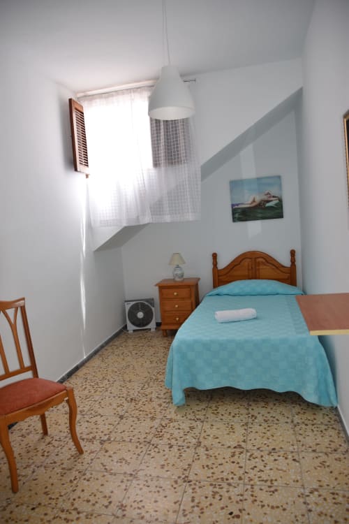 Habitación luminosa en la Pensión Eva de Puerto de Mogán con cama de madera, ropa de cama turquesa, piso de terrazzo y luz natural