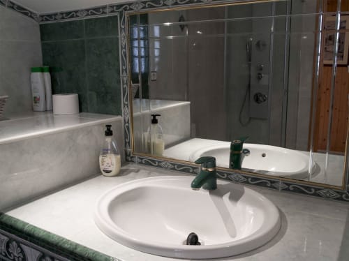 Baño moderno con lavabo blanco, detalles de mármol verde y ducha en Casa Rural Las Cuevas De Setenil, Cádiz