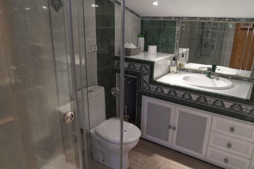 Baño moderno con ducha de cristal, tocador blanco y espejo decorativo en Casa Rural Las Cuevas De Setenil en Cádiz, España