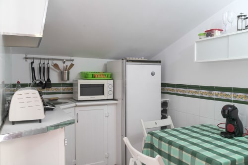 Cocina americana compacta en Casa Rural Las Cuevas De Setenil con muebles blancos, microondas, nevera y zona de comedor