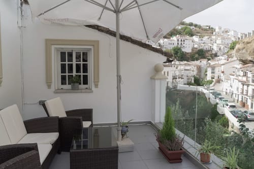 Terraza con muebles de mimbre y sombrilla con vistas a los edificios blancos de Setenil de las Bodegas, Cádiz