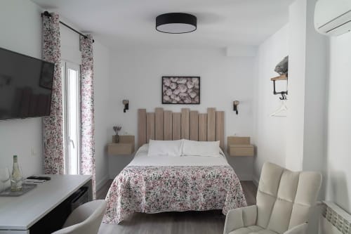 Habitación moderna de Casa Rural Las Cuevas De Setenil con colcha floral, cabecero de madera, TV y sillón beige