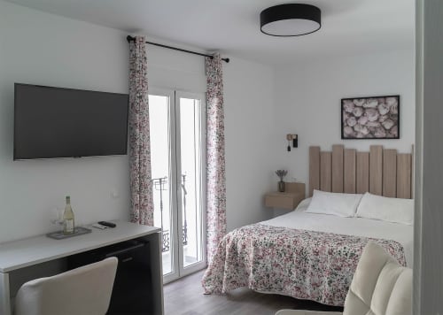 Moderno dormitorio en Casa Rural Las Cuevas De Setenil con TV, cortinas florales y vistas al río desde el balcón en Cádiz